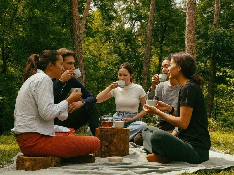 Grupa osób pijąca herbatę w kręgu w lesie